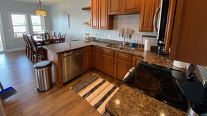 A modern kitchen with wooden cabinets, granite countertops, stainless steel appliances, and a dining area with a table and chairs. - Waterfront: Dock Access, Walk to Beach, Pier & Shops, 5BR, Sunset view / 10% off (Surf City)