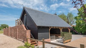 A small, modern building with a sloped roof, a brick exterior, and a wooden deck with outdoor seating. - Geoff's Rest with Hot Tub, Pond Hall Farm, Hadleig (Ipswich)