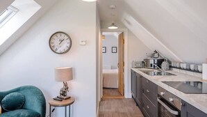A modern kitchen with a skylight, a clock, and a view into a bedroom. - Geoff's Rest with Hot Tub, Pond Hall Farm, Hadleig (Ipswich)