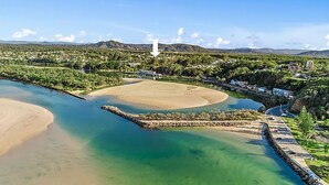 An aerial view of a coastal area with a sandy beach, clear waters, and a rocky breakwater. - With stunning ocean views and open living, enjoy the coastal lifestyle of Beauty on Bowra. (Nambucca Heads)