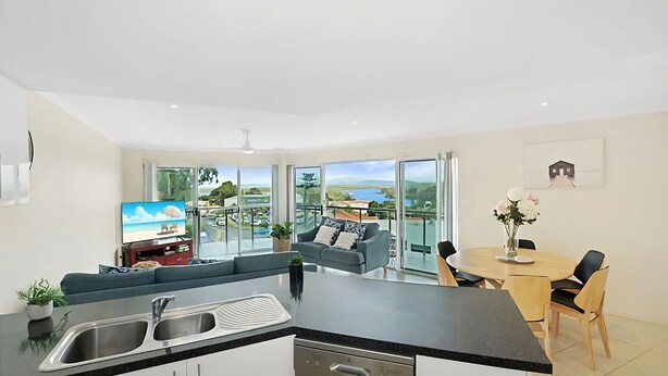 A modern kitchen with a dining area, large windows with a scenic view, and a flat-screen TV. - With stunning ocean views and open living, enjoy the coastal lifestyle of Beauty on Bowra. (Nambucca Heads)