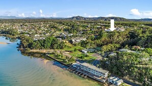 An aerial view of a coastal town with a prominent white tower, residential areas, and a marina. - With stunning ocean views and open living, enjoy the coastal lifestyle of Beauty on Bowra. (Nambucca Heads)