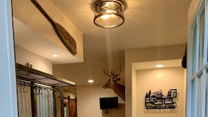 A cabin interior with a wooden bench, a deer head mounted on the wall, a television, and a welcome sign. - Home On Bike/Snowmobile/UTV-ATV Trail Near Chain of Lakes and Town! (Manitowish Waters)
