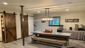 A rustic interior with a wooden barn door, a dining table with benches, a leather chair, and a 'GATHER' sign on the wall. - Home On Bike/Snowmobile/UTV-ATV Trail Near Chain of Lakes and Town! (Manitowish Waters)