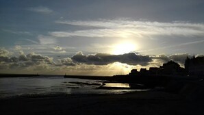 A coastal scene with a sunset, buildings, and a pier.