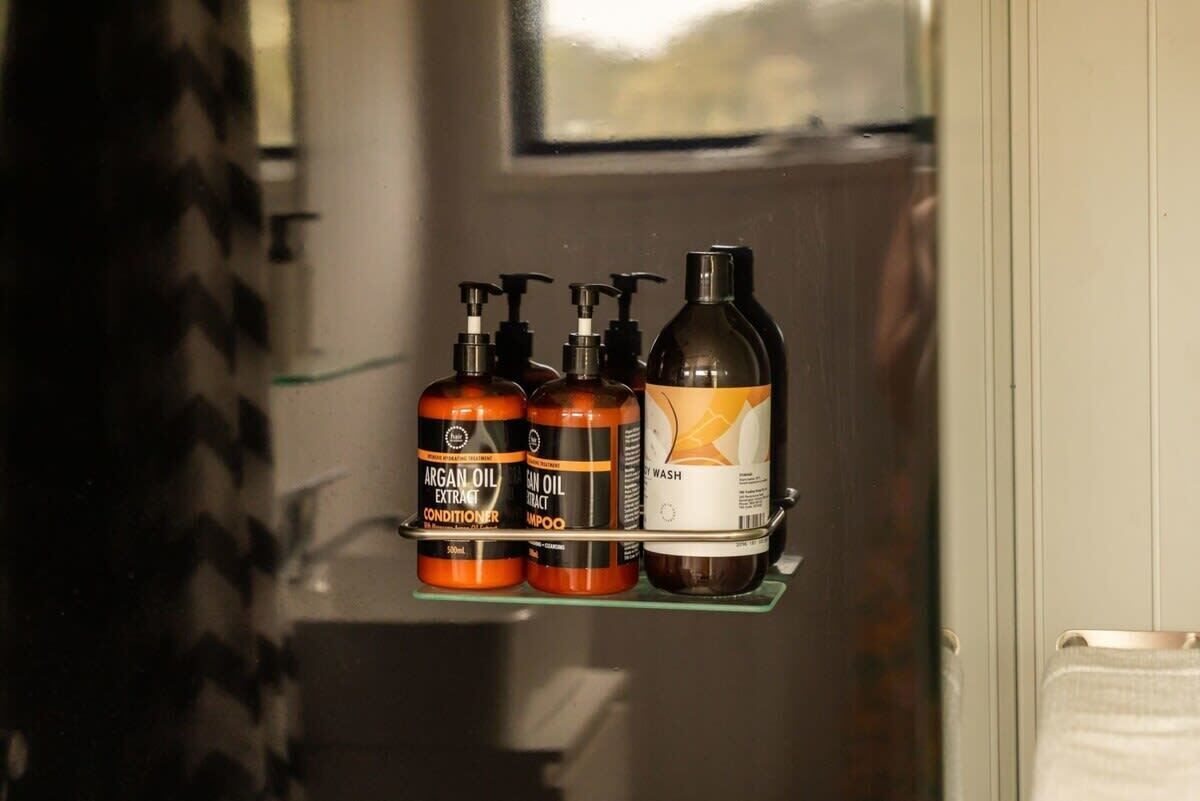 Een badkamerplank met drie flessen arganolieproducten en één fles vloeibare zeep.