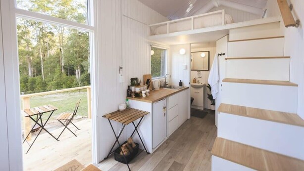 Une cuisine de taille réduite, dotée d’un plan de travail en bois, d’un évier et d’une fenêtre donnant sur une zone boisée.