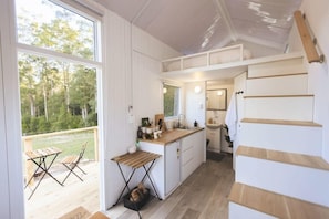 A compact kitchen with a wooden countertop, a sink, and a window overlooking a forested area. - Kookaburra Cabin 1 by Tiny Away (Palmwoods)