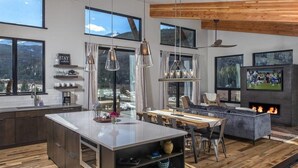 A modern kitchen with a central island, large windows with mountain views, and a cozy living area with a fireplace.