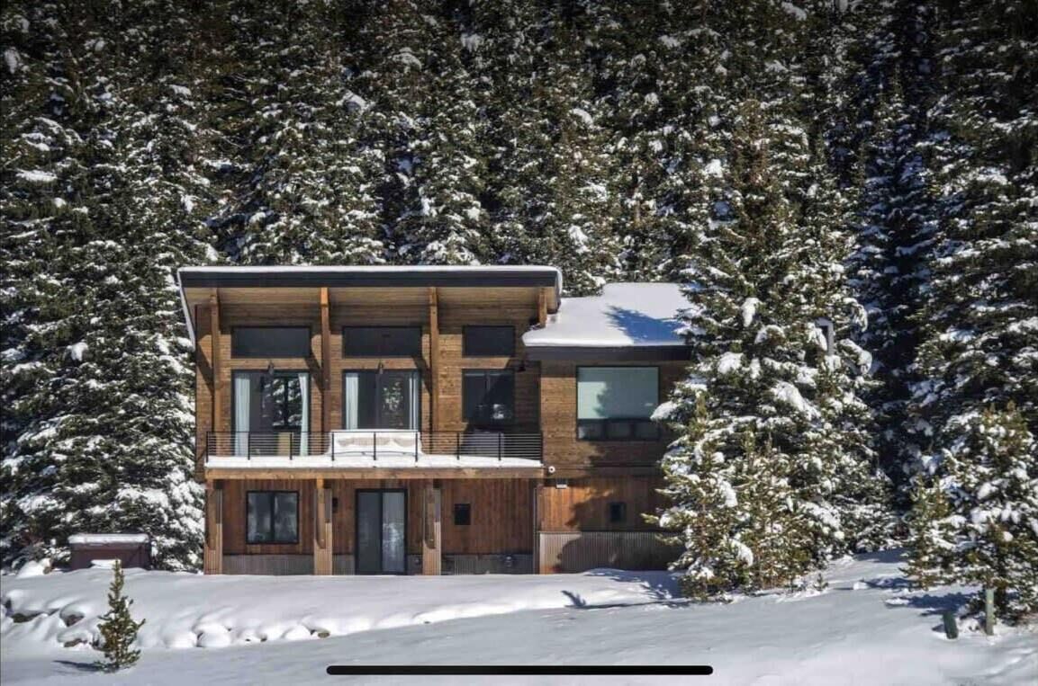 Eine moderne, zweistöckige Holzhütte, umgeben von schneebedeckten Bäumen.
