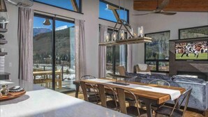 A modern dining area with a large table and chairs, a chandelier, and a view of a snowy landscape through large windows.