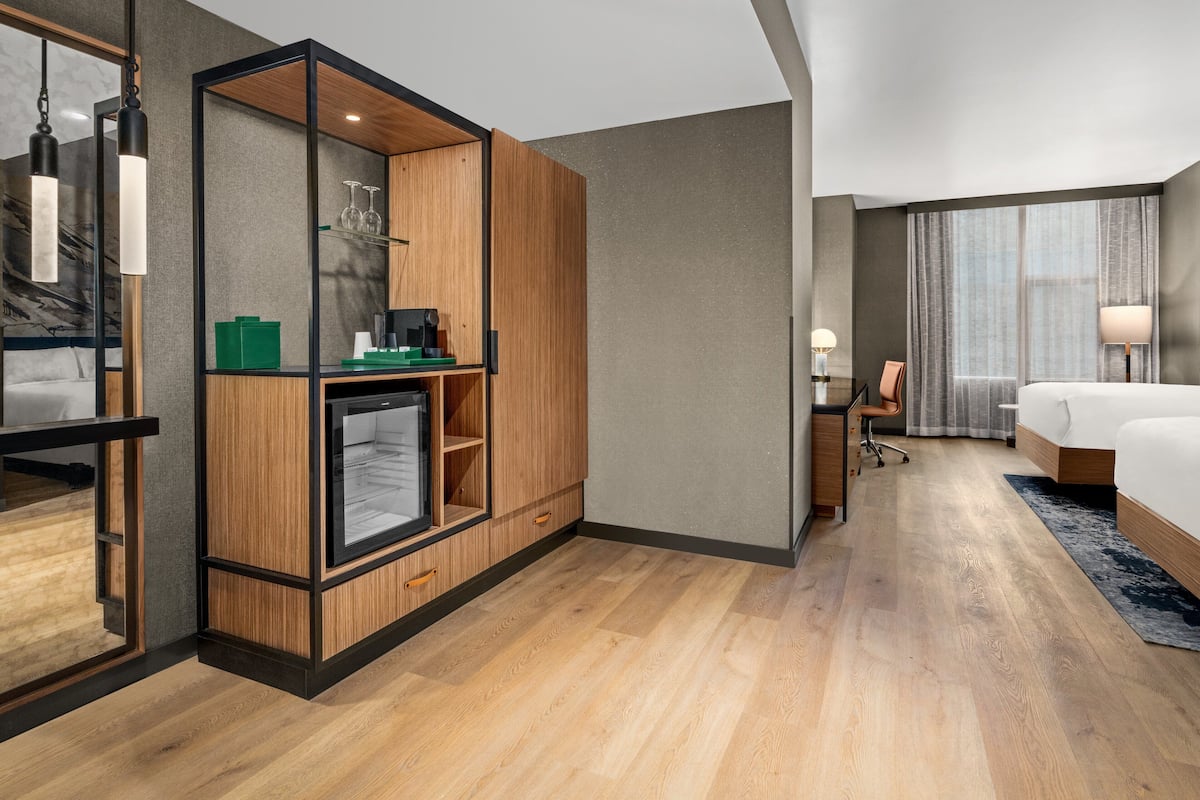 Een moderne hotelkamer met een houten garderobe, een bureau met stoel, een bed en een groot raam met gordijnen.