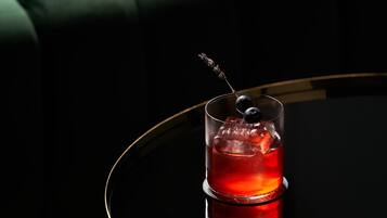 Un bicchiere con una bevanda rossa e un'oliva decorativa su una superficie riflettente.