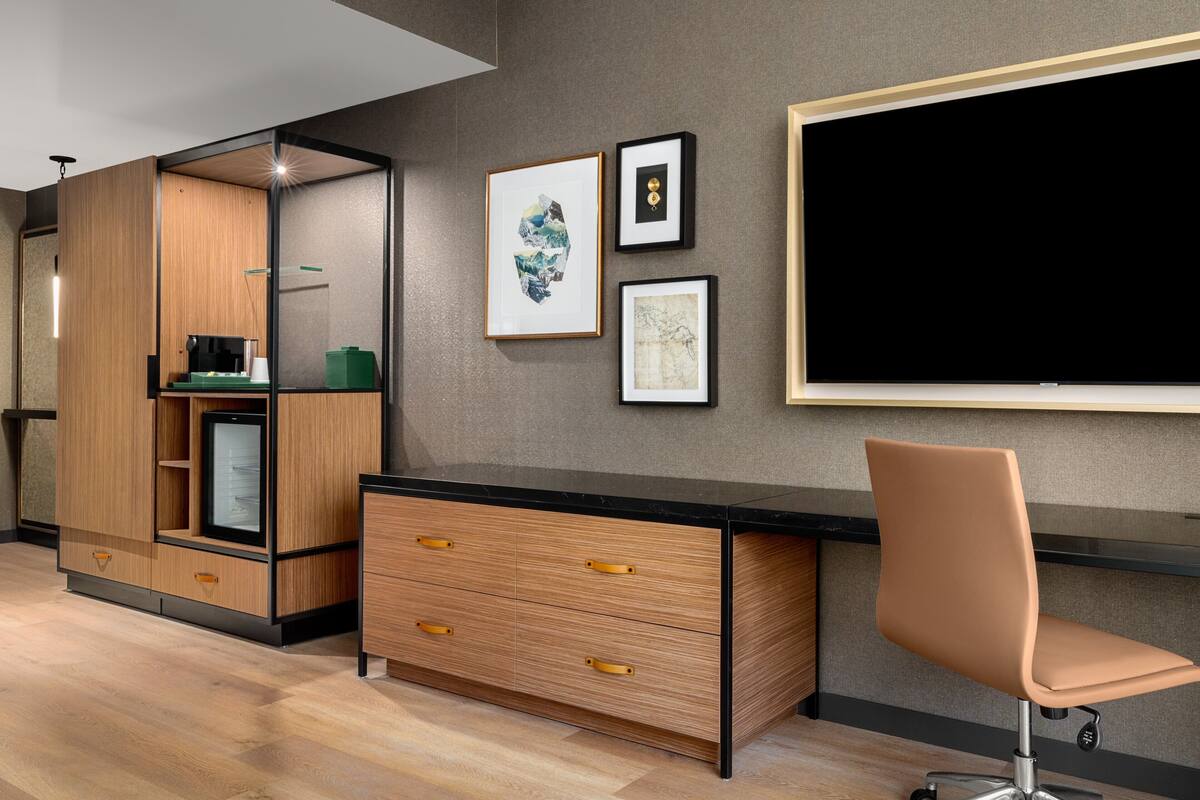 Een moderne kantoorruimte met een houten bureau, een stoel en een koelkast. Er hangen ingelijste foto's aan de muur.