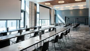 Un salón de conferencias con mesas largas, sillas y una pantalla grande.