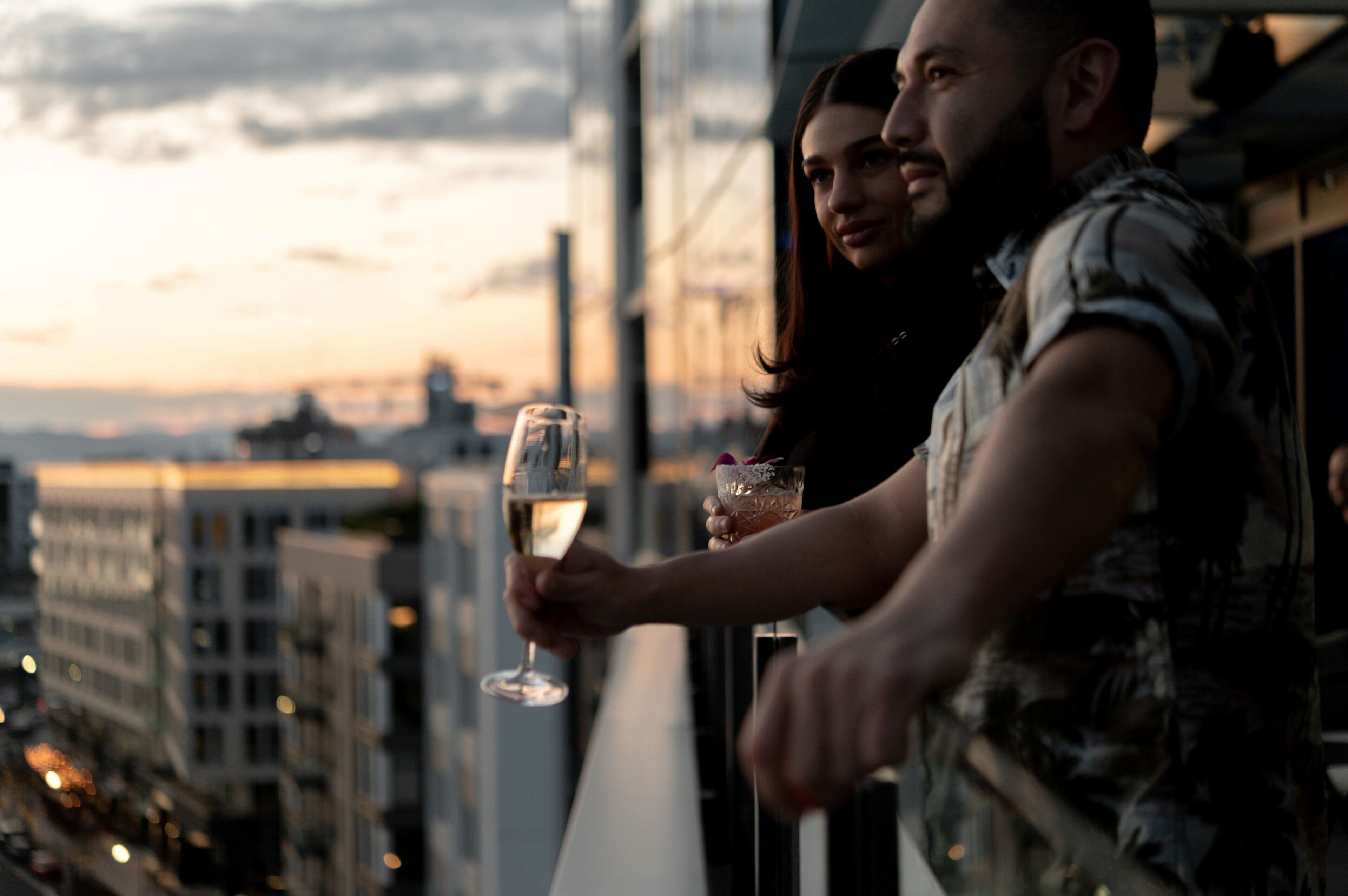 A person holding a glass of wine, standing by a window with a cityscape view.