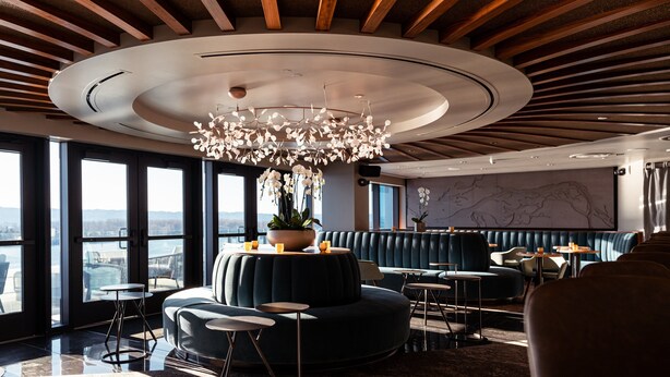 Een modern interieur met een rond plafondontwerp, een centrale kroonluchter, zithoeken en grote ramen met uitzicht.