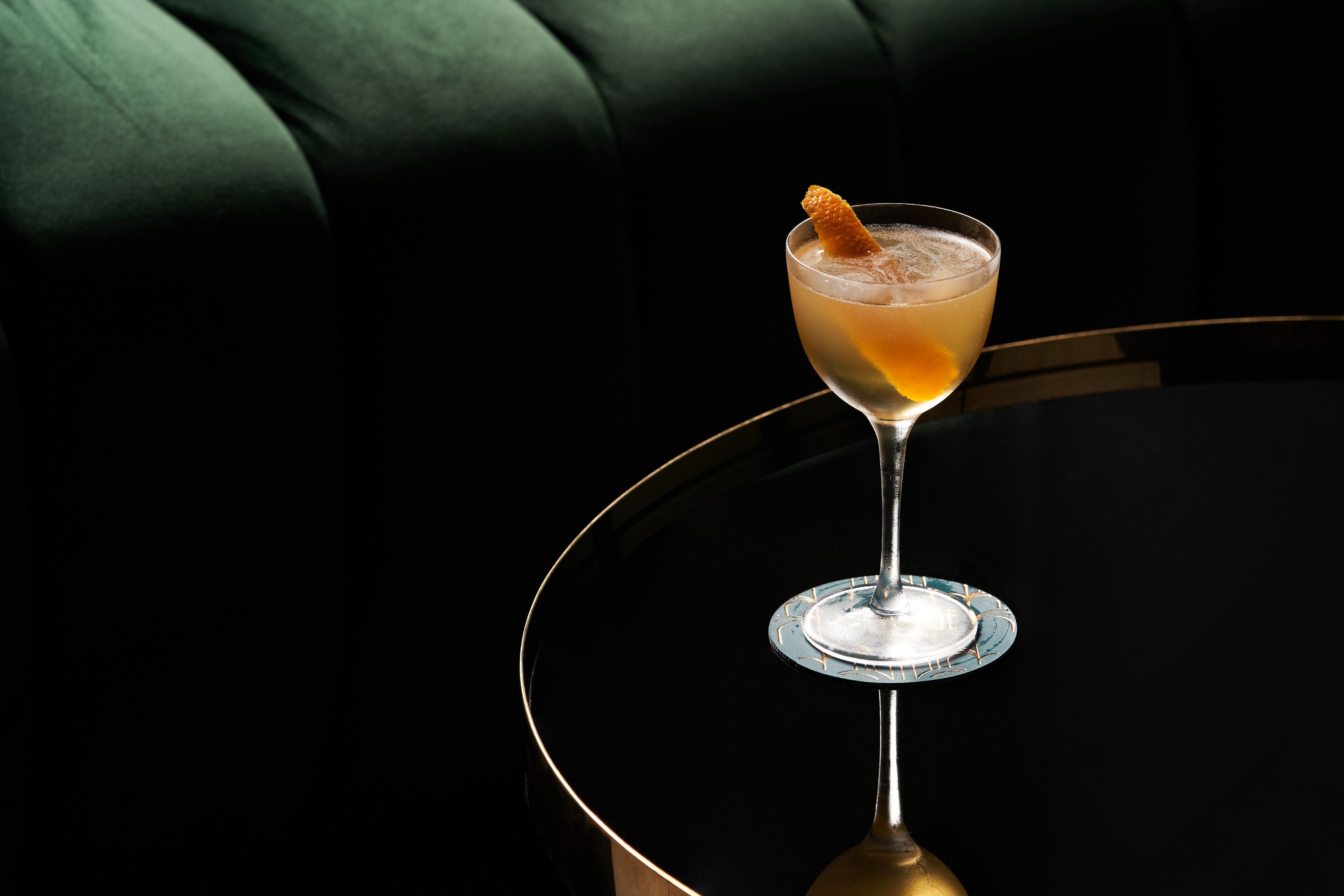 A cocktail in a glass on a round table with a black surface.