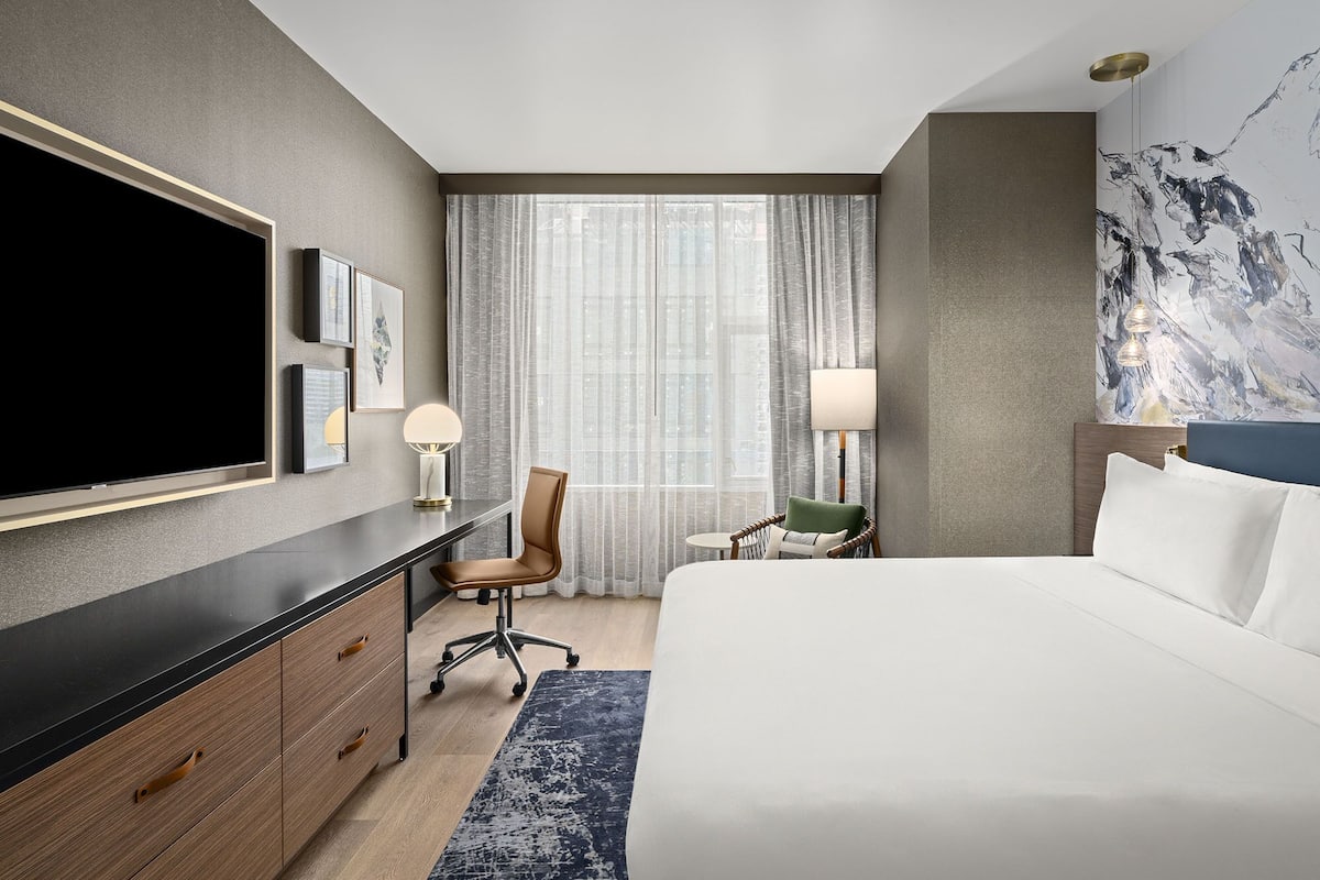 Een hotelkamer met een bed, een bureau met een televisie, een stoel, een lamp en een schilderij aan de muur.