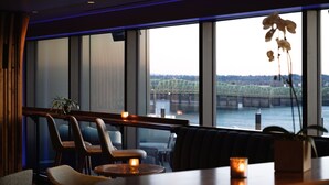 Een restaurant met uitzicht op een brug en rivier, met moderne zitplaatsen en kaarsen.