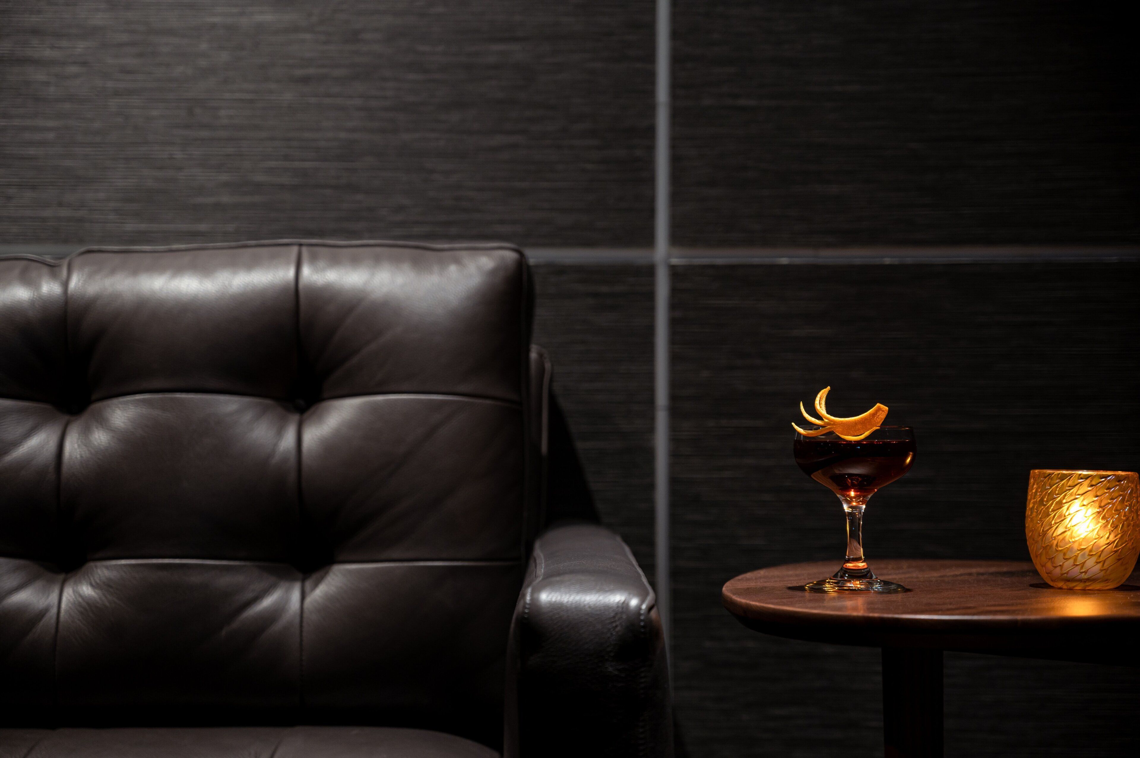 Een donker lederen fauteuil en een klein rond tafeltje met een glas en een gouden schaal.