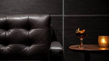 Een donker lederen fauteuil en een klein rond tafeltje met een glas en een gouden schaal.