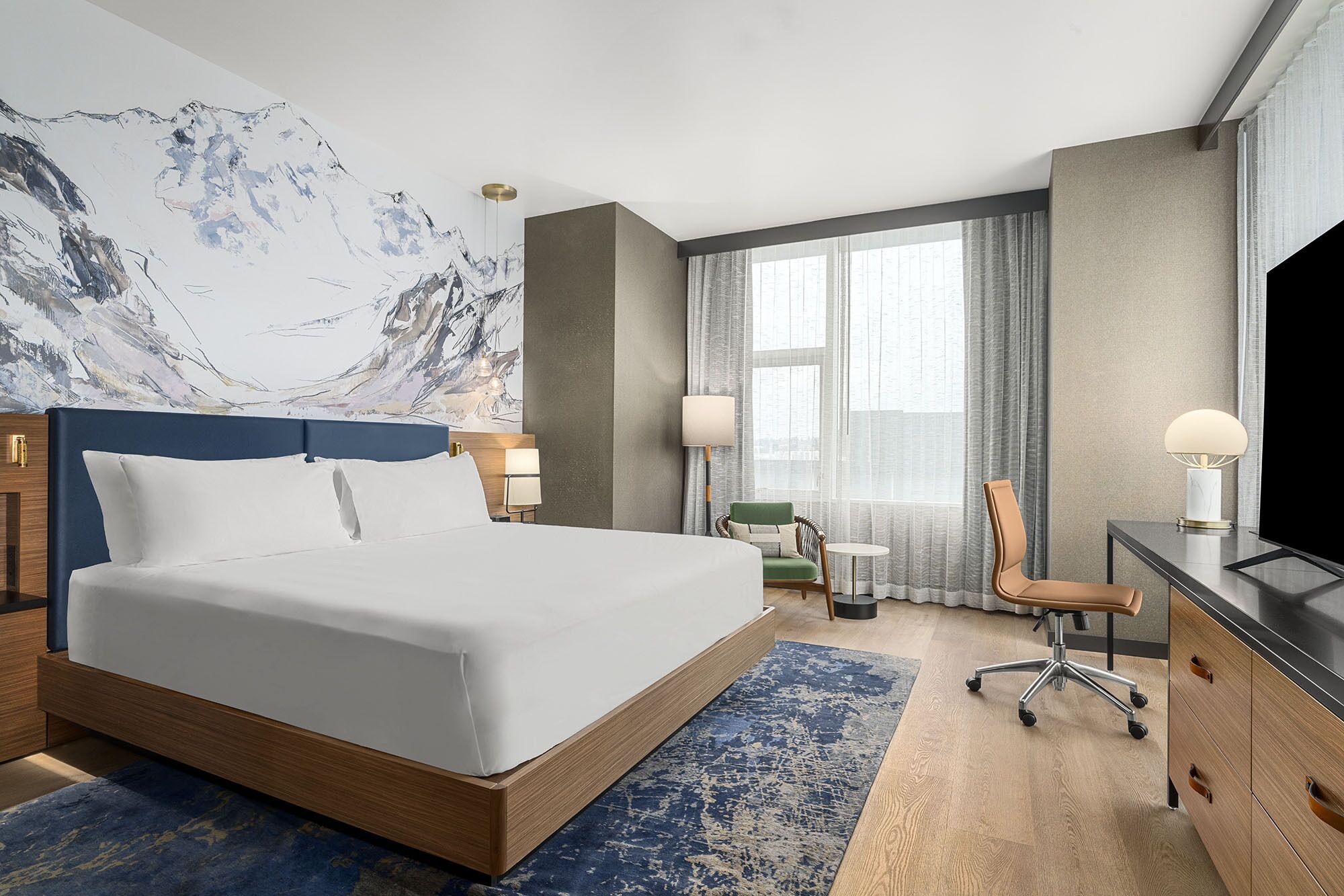 A hotel room with a large bed, a desk with a chair, a television, and a window with curtains.