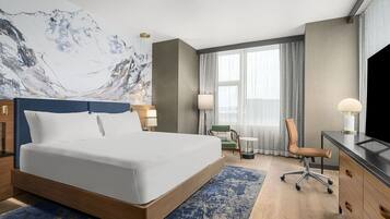 A hotel room with a large bed, a desk with a chair, a television, and a window with curtains.