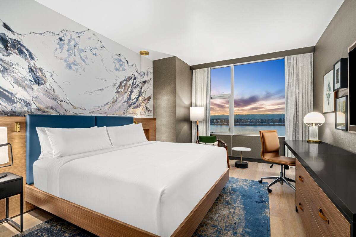 Een hotelkamer met een groot bed, een bureau, een stoel en uitzicht op de stadsbelangrijkste punten.