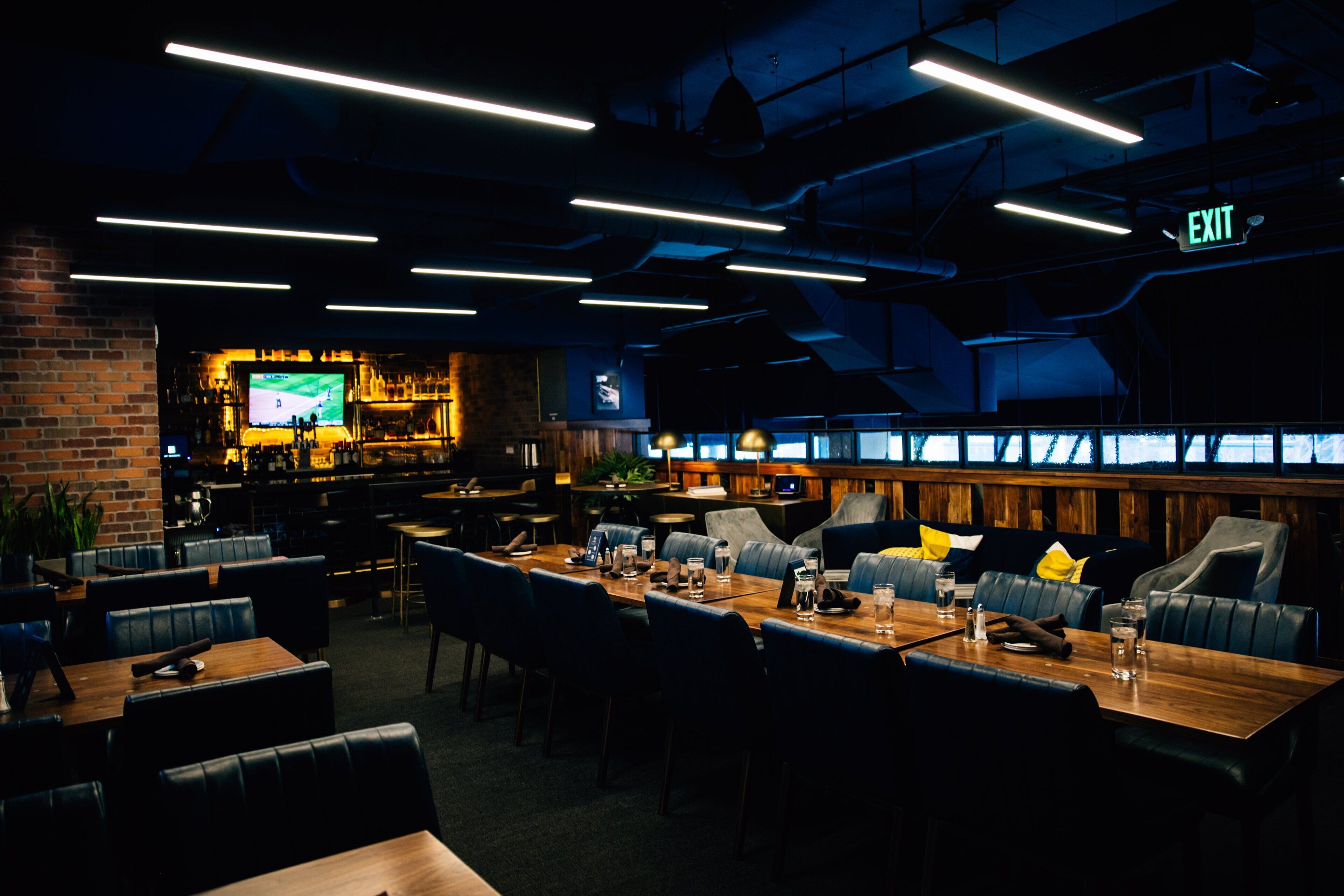 A modern restaurant with a bar area, wooden tables, and leather seating.