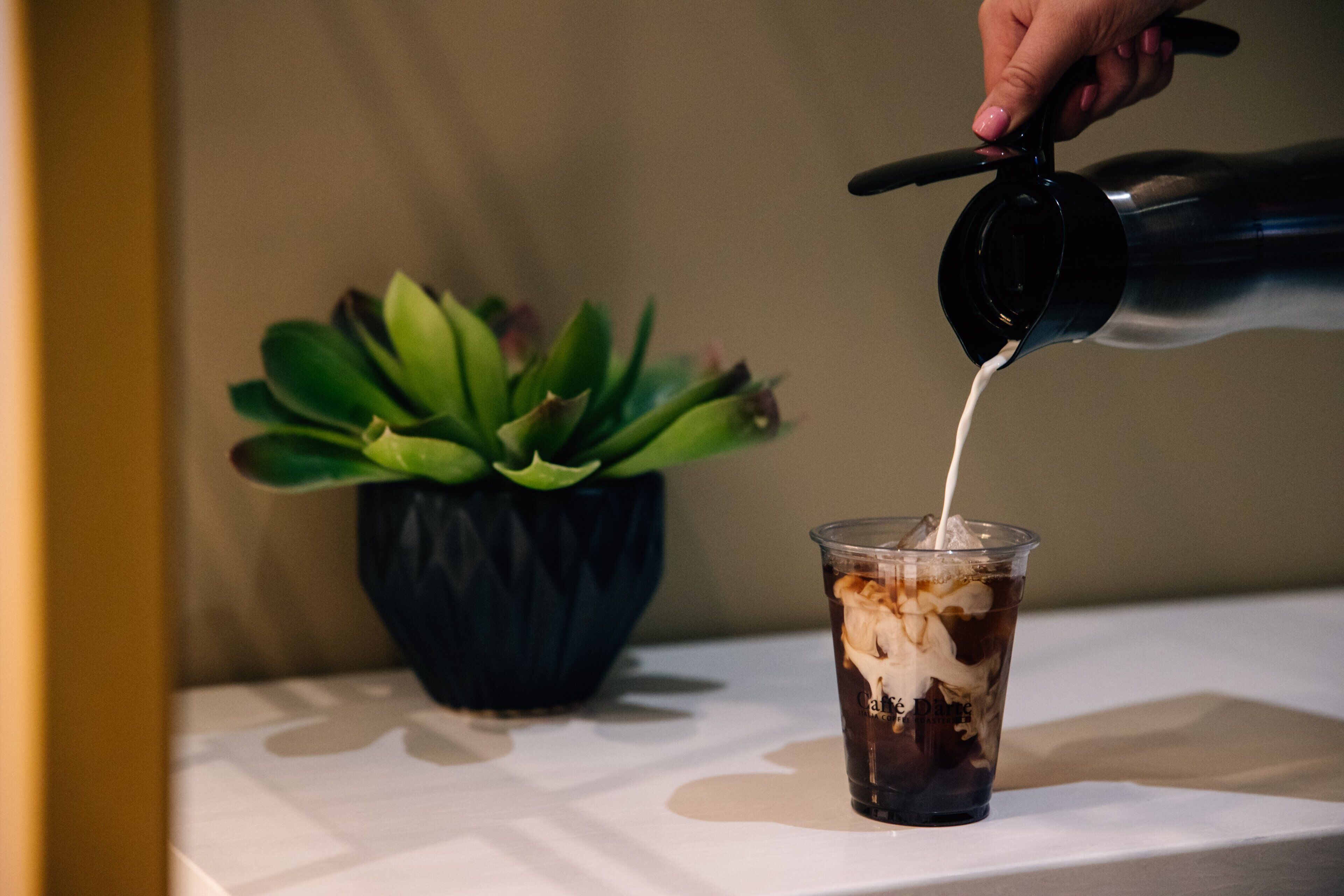 A hand pouring milk into a glass of iced coffee.
