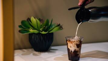 A hand pouring milk into a glass of iced coffee.
