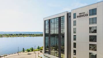 Un hôtel moderne doté de grandes fenêtres, offrant une vue sur un lac, et dont l’enseigne « HOTEL INDIGO » est affichée sur le bâtiment.