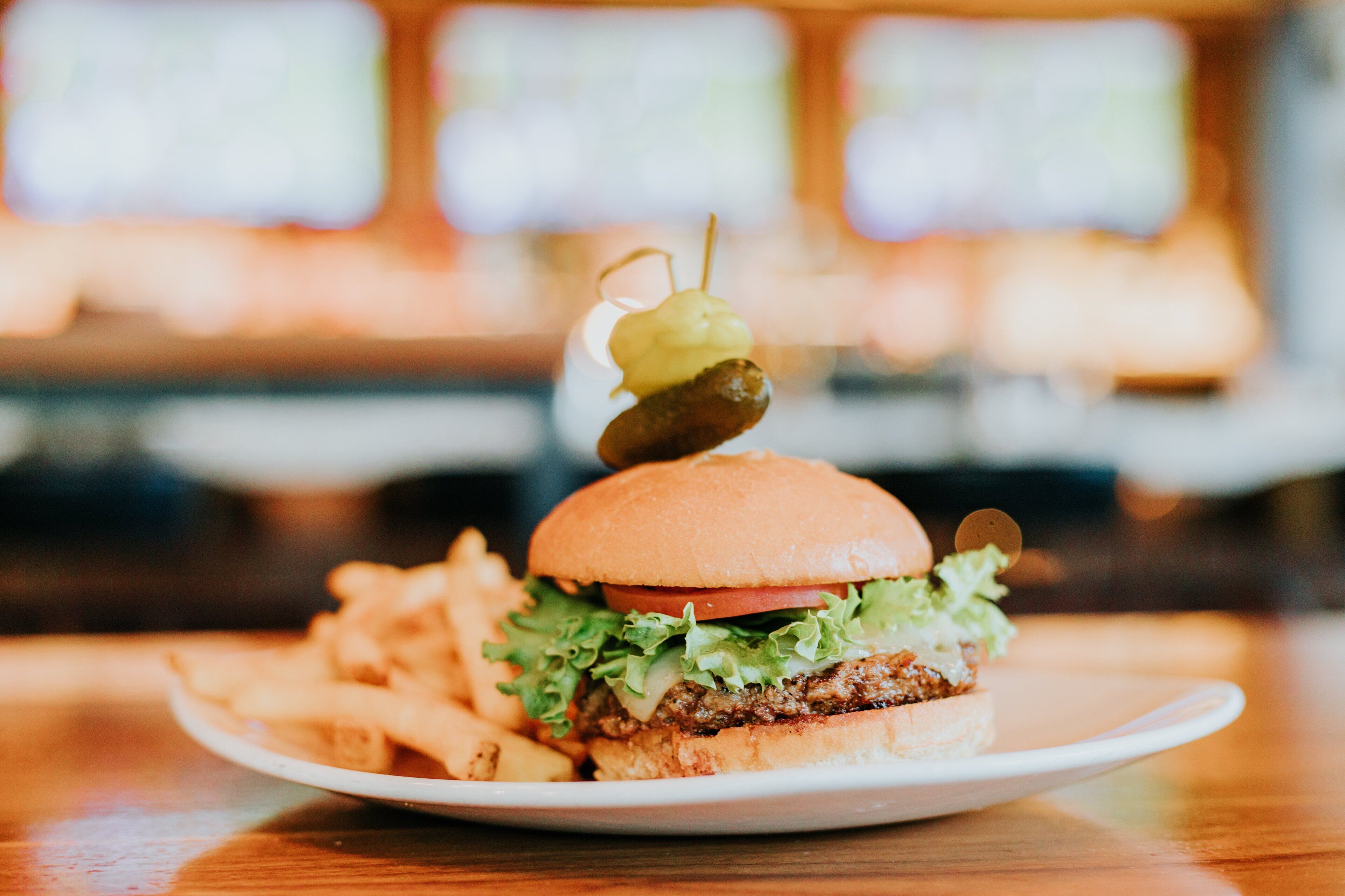 Un hamburger avec un cornichon, servi dans un pain, accompagné de frites sur une assiette blanche.