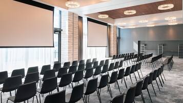 Una sala de conferències amb files de cadira, grans finestres i una pantalla projectora.