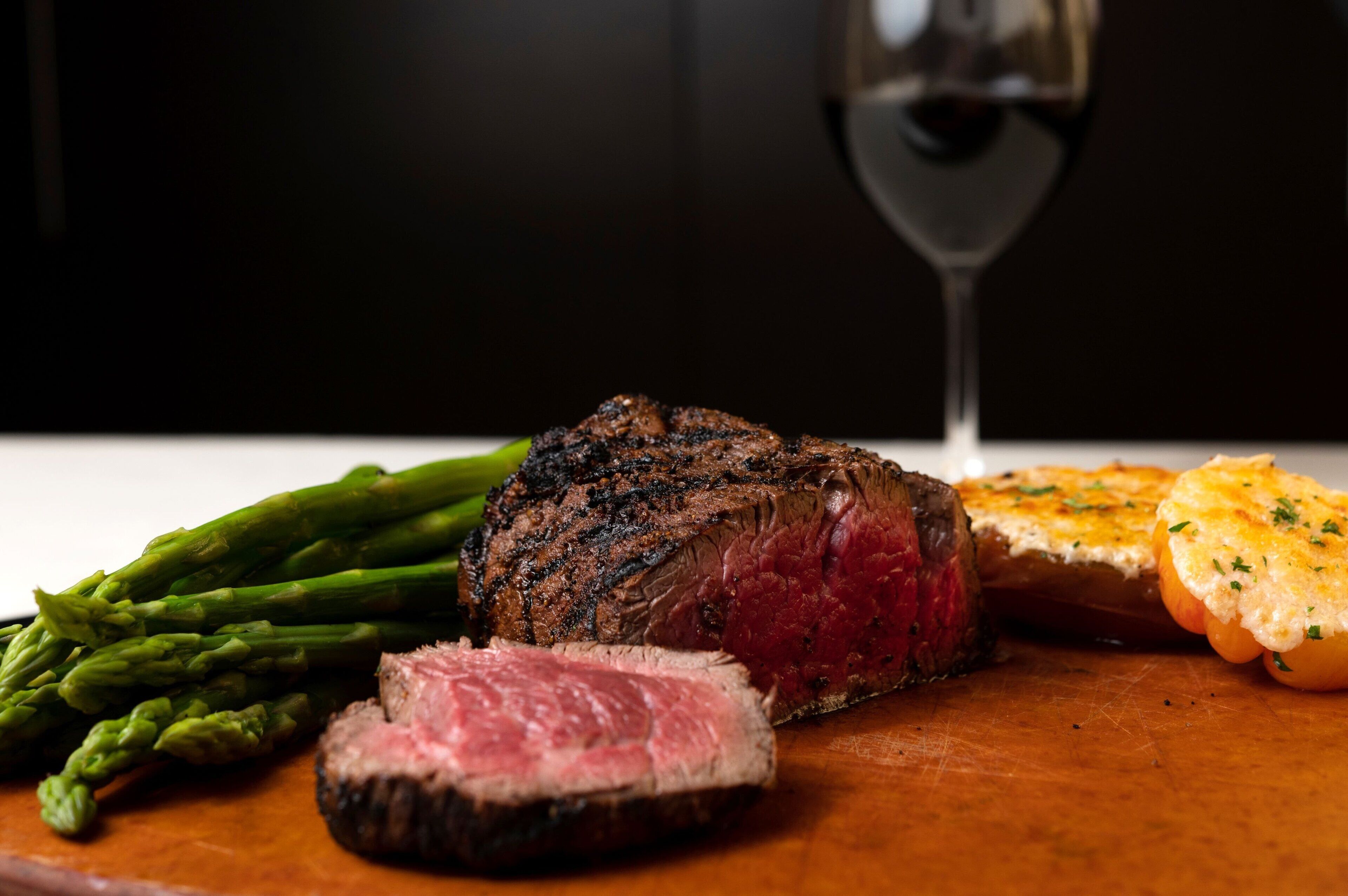 A steak with asparagus and garlic bread on a wooden board.