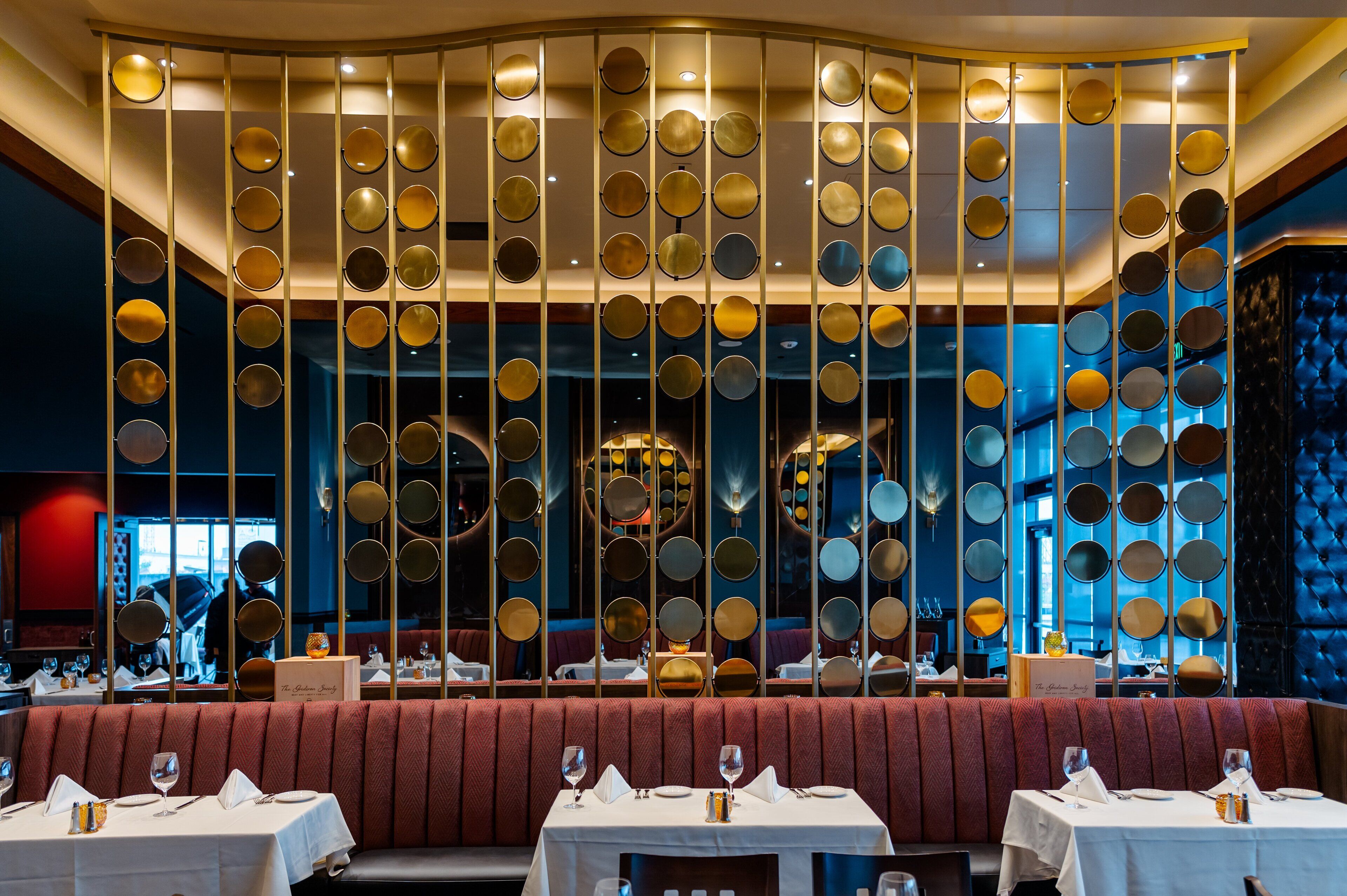 Ein Restaurant mit modernem Ambiente, das eine Wand mit runden Spiegeln und eine Sitzgruppe mit roter Polsterbank zeigt.