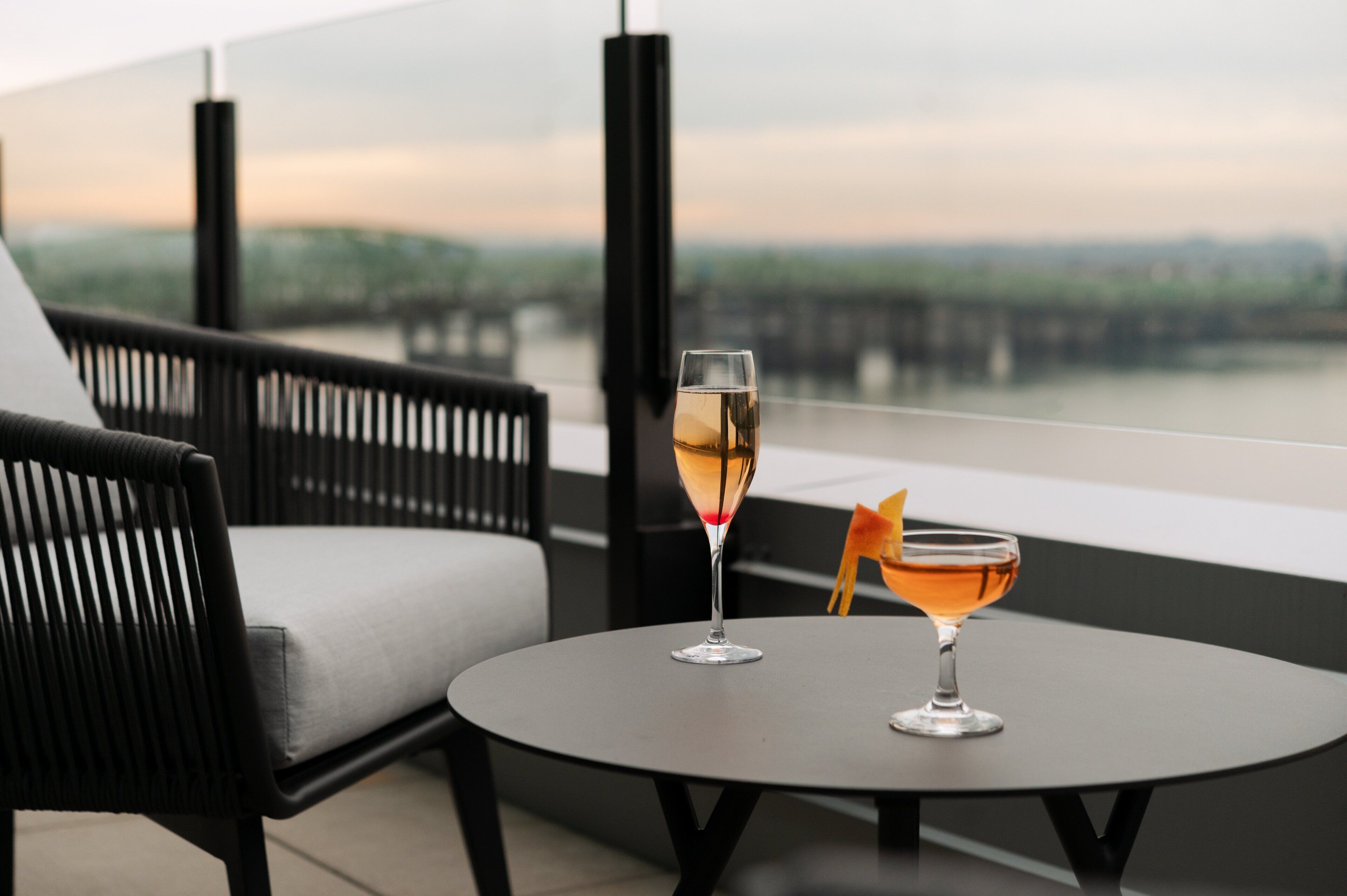 Ein Balkon mit einem runden Tisch, zwei Gläsern Getränke und einem Korbstuhl.