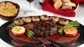 Een steak met gegrilde champignons en asperges op een bord, vergezeld van een soepkom en een glas rode wijn.