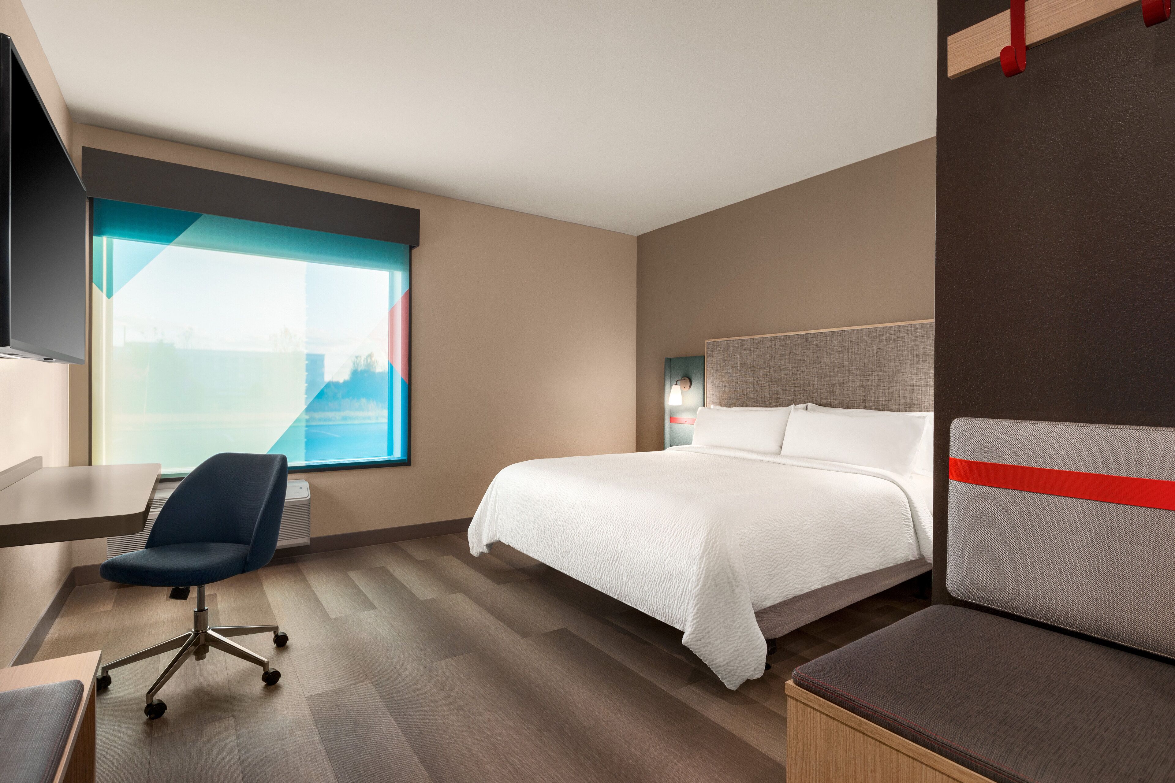 Ein Hotelzimmer mit Bett, Schreibtisch, Stuhl und großem Fenster.