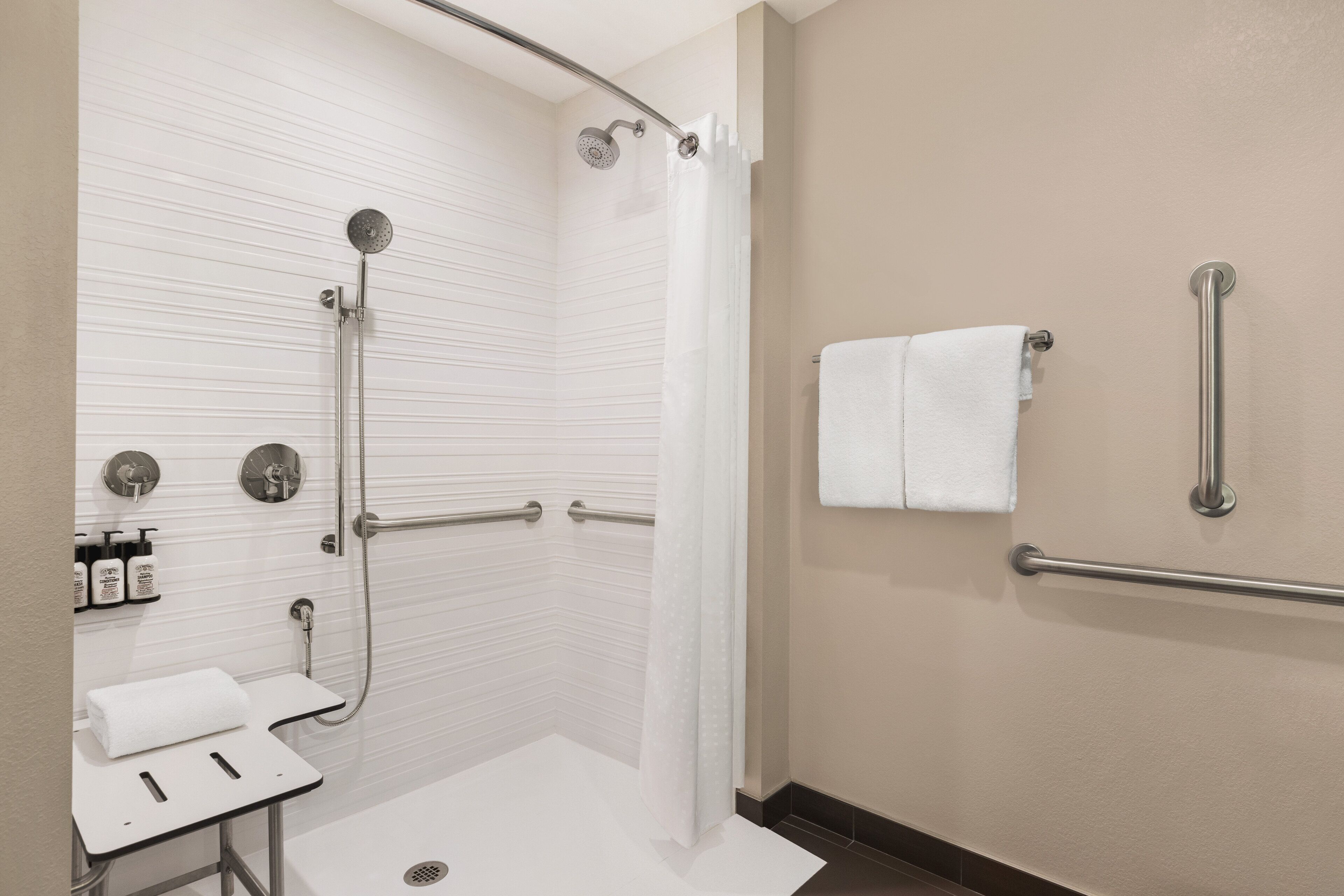 A modern bathroom with a shower, grab bars, a sink, and a towel rack.