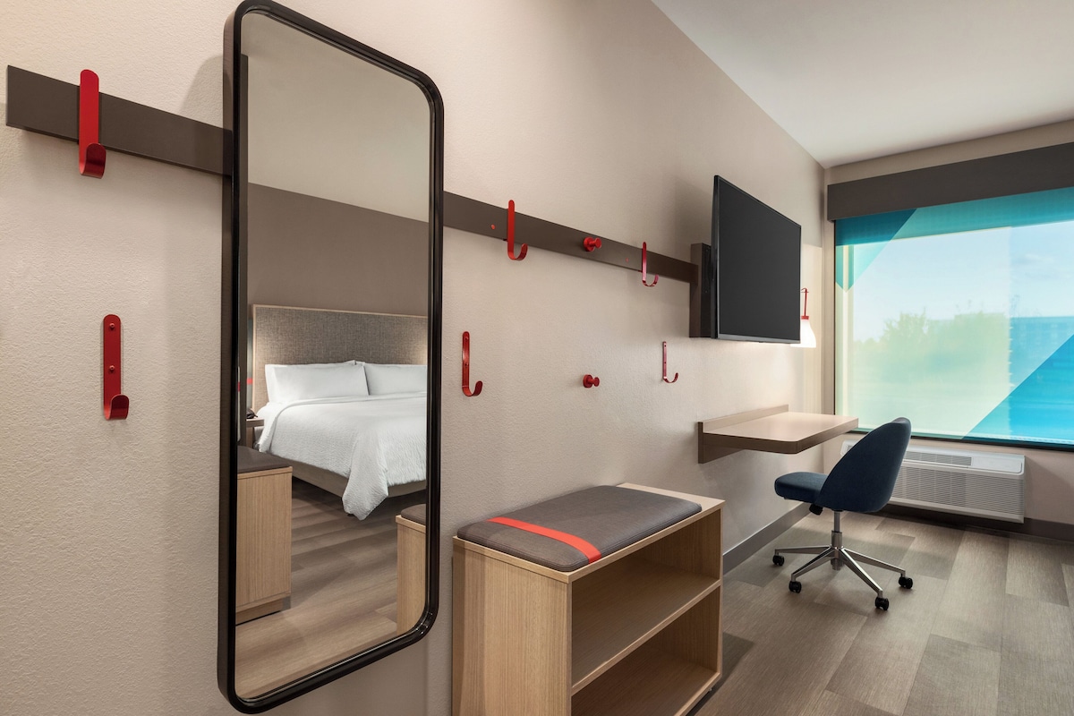 Moderni hotellihuone, jossa on sänky, työpöytä, tuoli, televisio ja suuri ikkuna.