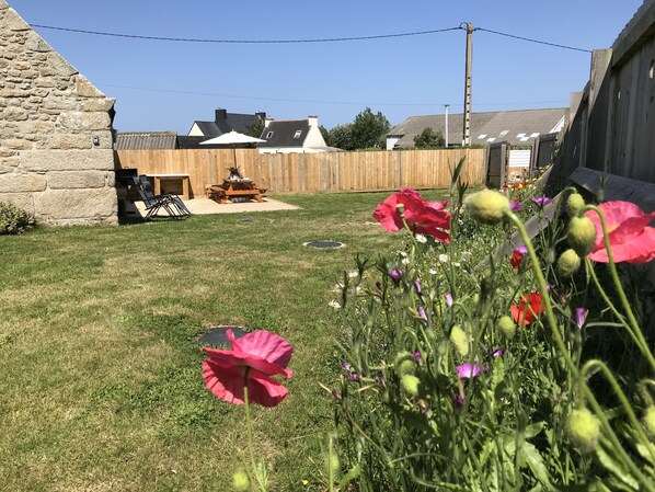 Ein Garten mit Holzzaun, Picknicktisch und verschiedenen Blumen.