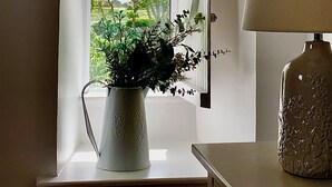 Une pièce avec une fenêtre, un vase blanc contenant une plante et une lampe posée sur une table.