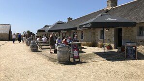 Un espace de restauration en plein air au style rustique, agrémenté de bâtiments en pierre, de barils en bois et de parasols noirs.