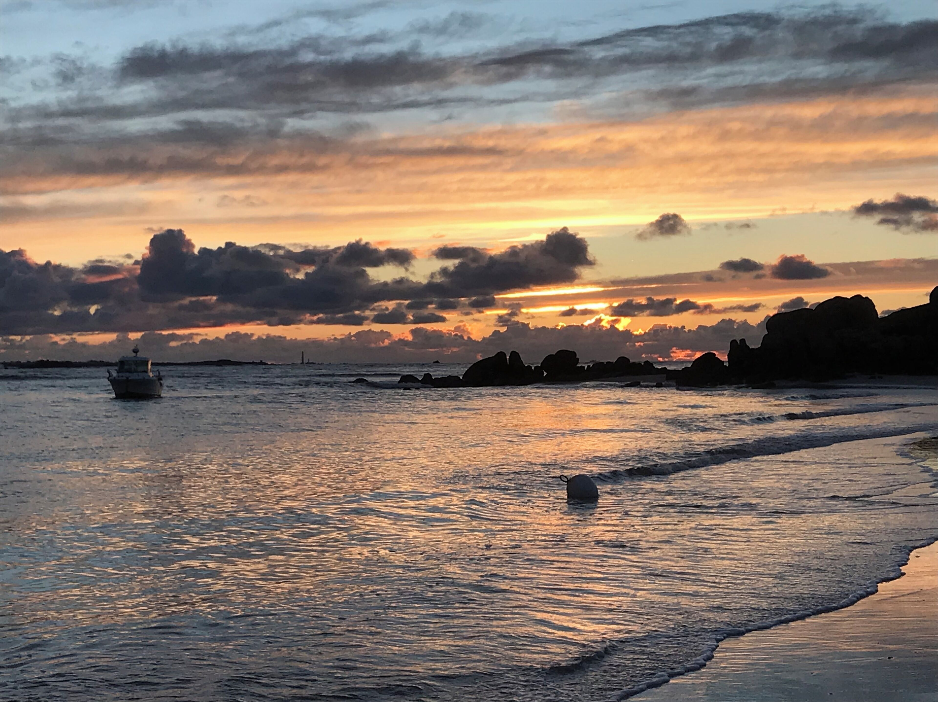 Ein Sonnenuntergang über einem ruhigen Meer mit einem Boot in der Ferne und Felsformationen am Ufer.