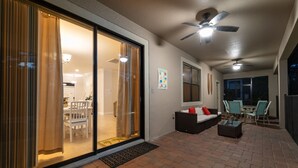 Un espace patio extérieur doté d’une porte-fenêtre coulissante donnant sur un coin repas, d’un canapé avec des coussins, d’une table basse et de ventilateurs de plafond.