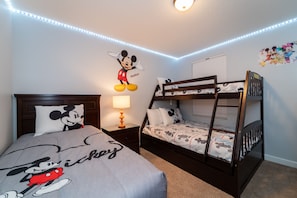 Une chambre avec un lit superposé, un autocollant mural à l’effigie de Mickey Mouse et des bandes lumineuses à LED le long du plafond.