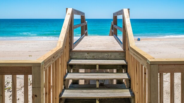 Una passerella di legno che conduce a una spiaggia con acque cristalline e una riva sabbiosa.