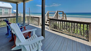 Un pontile in legno con due poltrone Adirondack, una ringhiera in legno e vista sulla spiaggia e sull'oceano.
